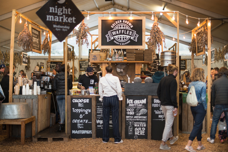 A group of people enjoying the Oranjezicht City Farm Market at night.